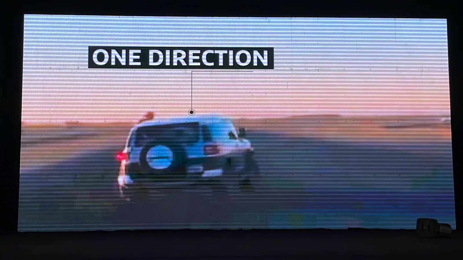 The LED wall showing a 4x4 driving across sand, labelled One direction.