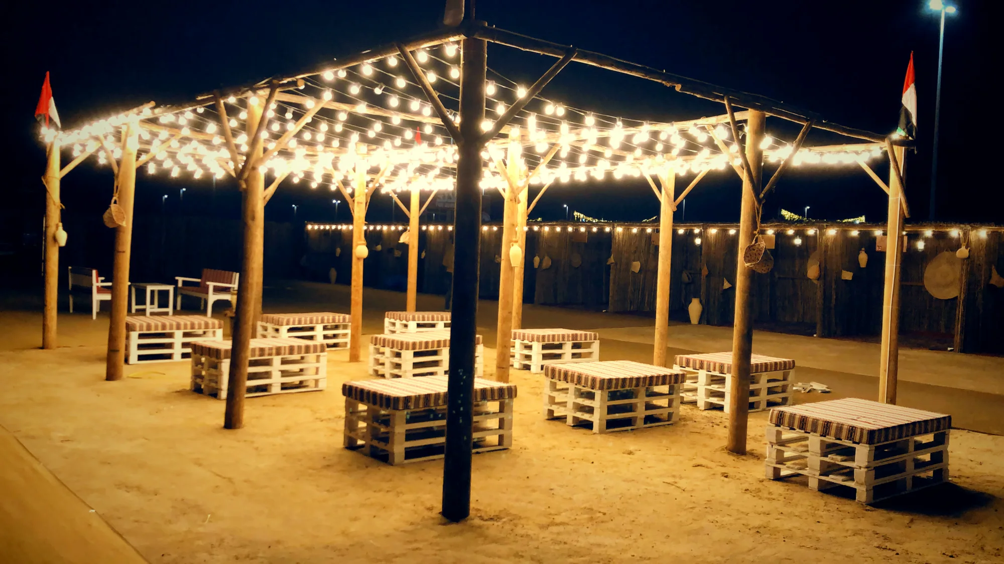 The pergola, lit: strings of bulbs over pallet seating on the sand